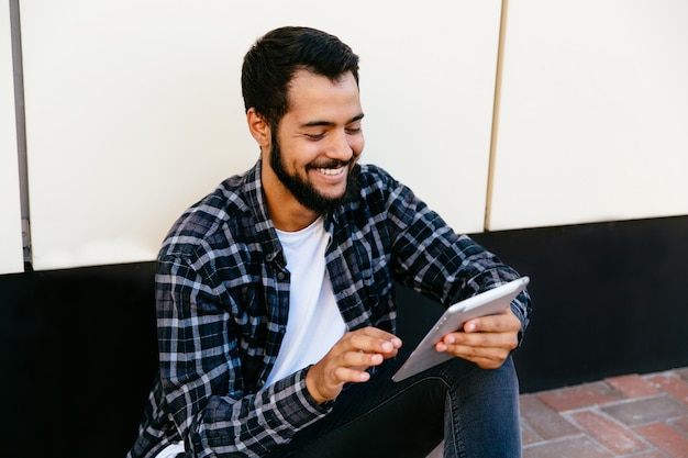 Stylish young hipster man using a digital tablet , cheerfully smiling, looking at tablet screen