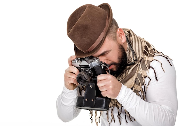 Stylish young male photographer with retro camera takes photos on white background