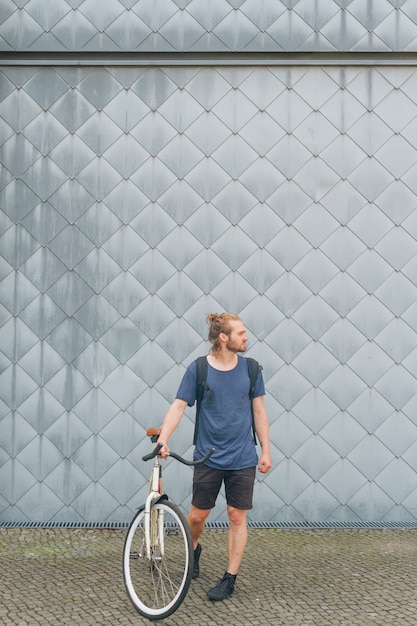 Stylish young man carrying backpack standing with his bicycle