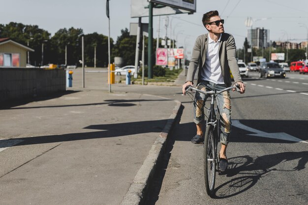 Stylish young man riding bicycle on street