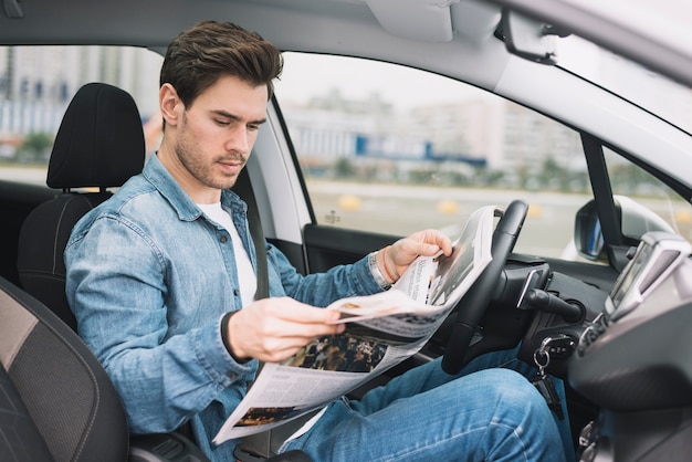 Stylish young man sitting in the luxury car reading newspaper