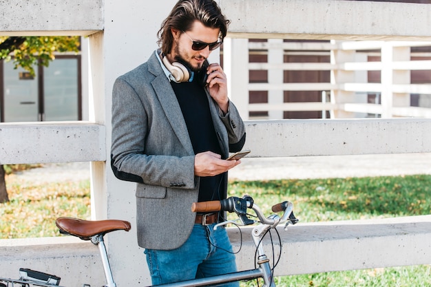 Stylish young man standing near the bicycle using mobile phone