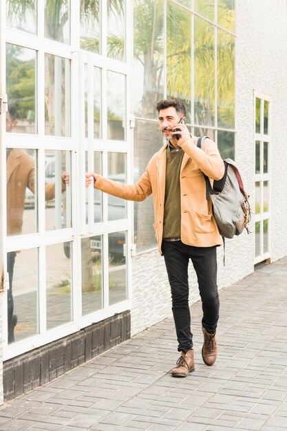 携帯電話で話している建物の外に立っているスタイリッシュな若い男