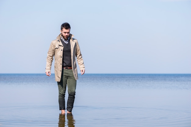 Stylish young man walking in the shallow sea water against blue sky