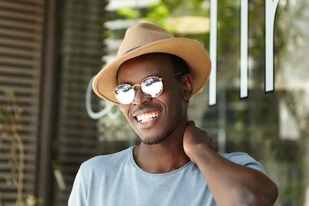 Elegante giovane uomo che indossa cappello e occhiali da sole