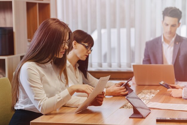 Stylish young people in the modern office work at one desk with documents and a laptop