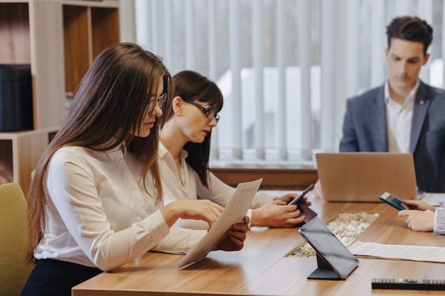 Stylish young people in the modern office work at one desk with documents and a laptop