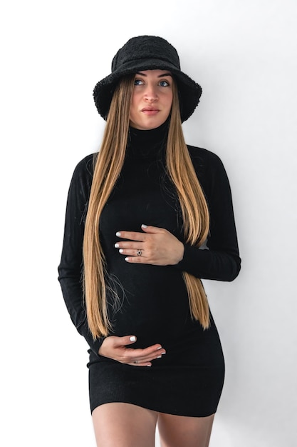 Stylish young pregnant woman in a black short dress on a white background