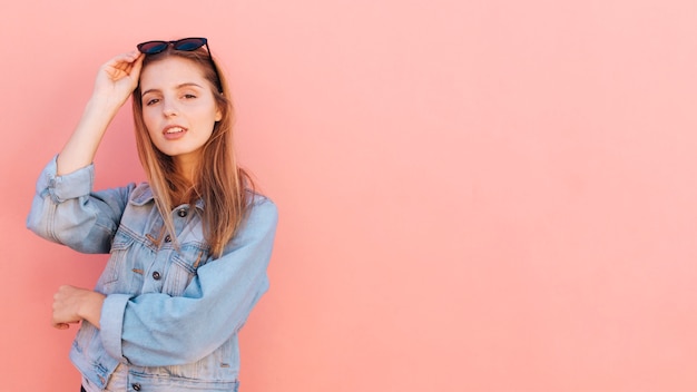 Stylish young woman in blue denim jacket standing against pink backdrop