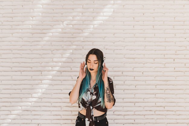 Stylish young woman enjoying listening music on headphone against beige wall