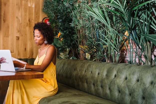 Stylish young woman looking at documents with laptop on wooden table in the restaurant