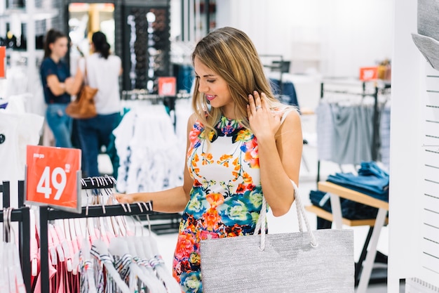 Stylish young woman looking at dress hanging on rack in the showroom