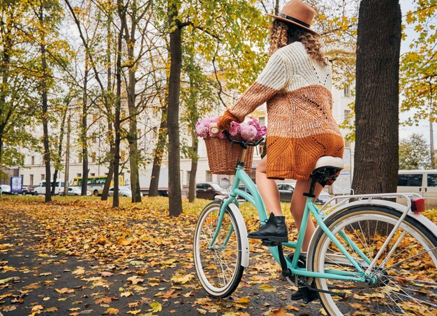 Stylish young woman riding bicycle with flowers on autumn street