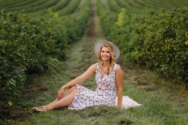 Stylish young woman in rose blue vintage dress and hat posing in green field