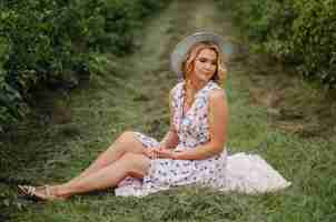 Free photo stylish young woman in rose blue vintage dress and hat posing in green field