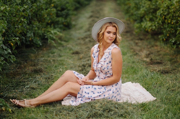 Stylish young woman in rose blue vintage dress and hat posing in green field