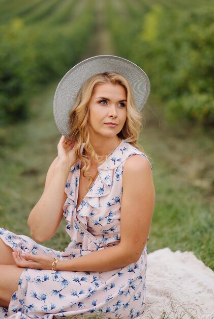 Stylish young woman in rose blue vintage dress and hat posing in green field