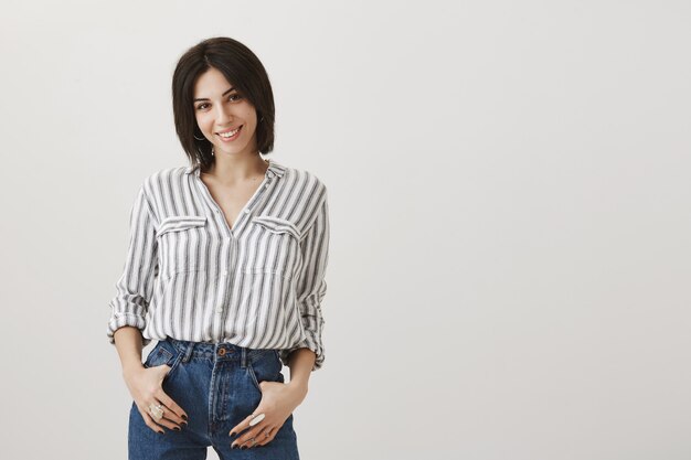 Stylish young woman smiling, holding hands in pockets confident