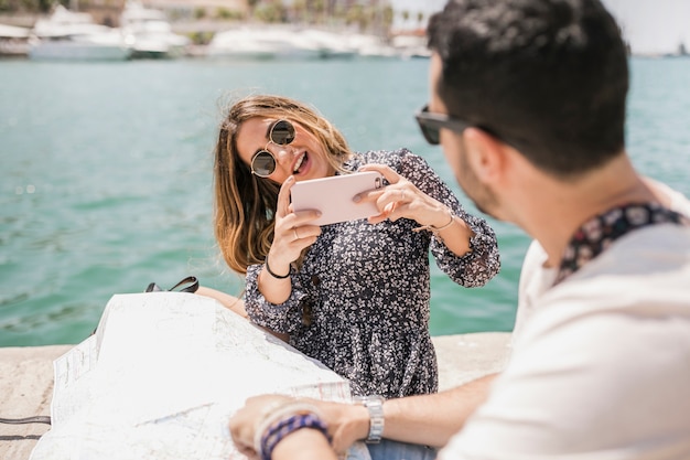 Free photo stylish young woman taking picture of her boyfriend on jetty