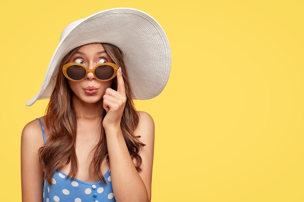 Free photo stylish young woman wearing a hat posing against the yellow wall