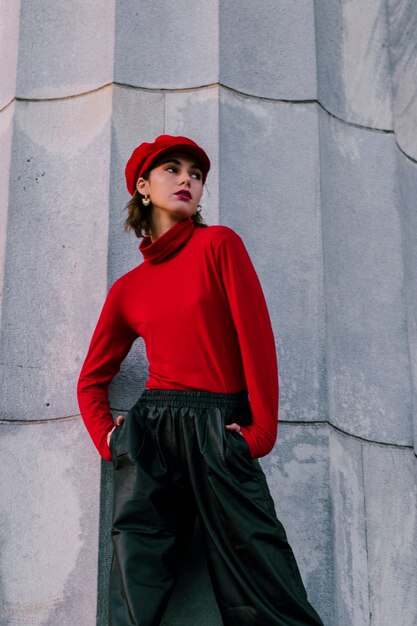 Стильная молодая женщина в красной кепке с руками в кармане смотрит в сторону