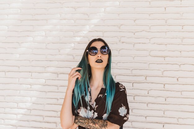 Stylish young woman with dyed hair standing in front of beige wall