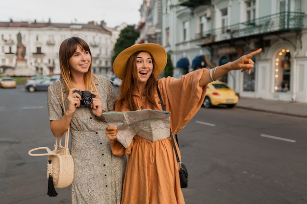 Free photo stylish young women traveling together in europe dressed in spring trendy dresses and accessories