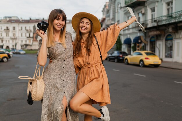 Stylish young women traveling together in Europe dressed in spring trendy dresses and accessories