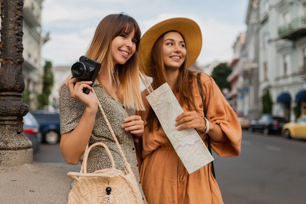 Stylish young women traveling together in Europe dressed in spring trendy dresses and accessories