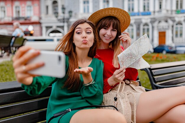 Stylish young women traveling together in Europe dressed in spring trendy dresses and accessories
