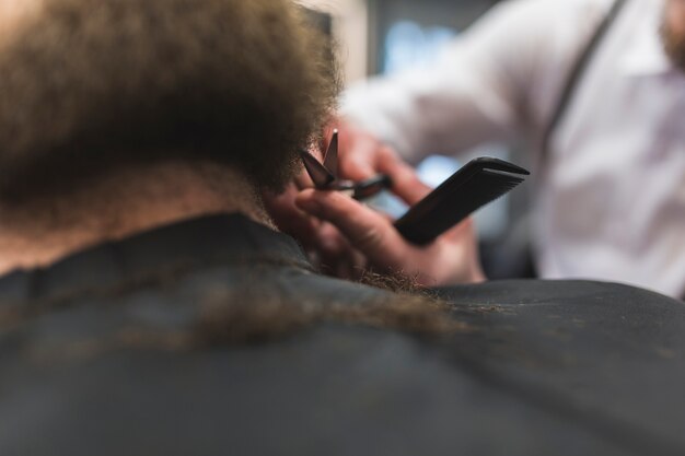 Stylist cutting beard of faceless client