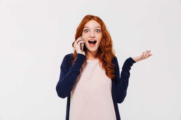 Su rprised beautiful young redhead lady talking by mobile phone.