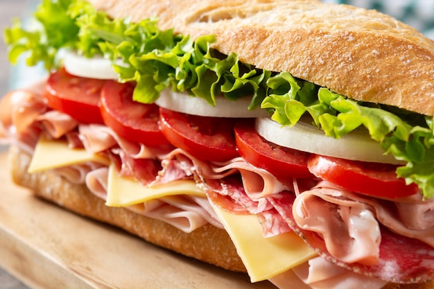 Submarine sandwich with ham cheese lettuce tomatoesonion mortadella and sausage on wooden table