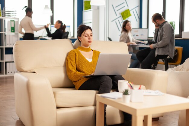 居心地の良いソファに座ってスタートアッププロジェクトでラップトップに取り組んで成功したビジネス女性