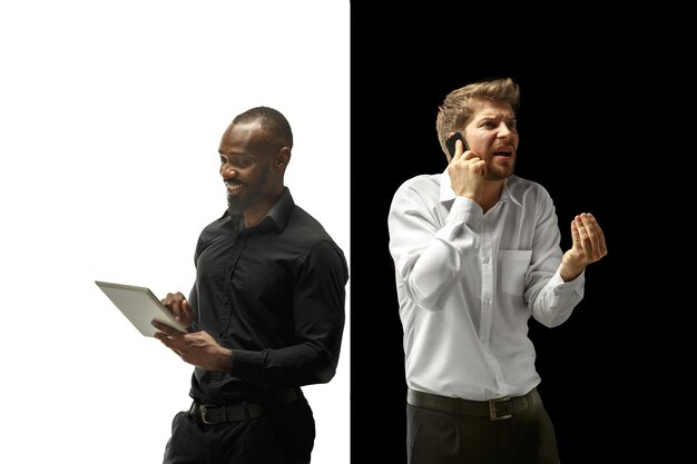 The success happy afro and caucasian men. Mixed couple with gadget. Dynamic image of male models on white and black studio. Human facial emotions concept.