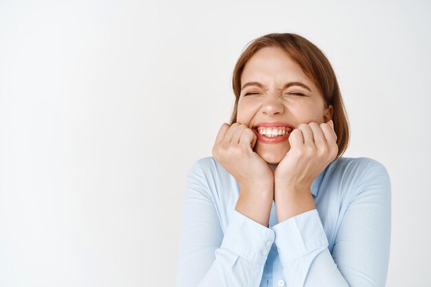 Success Happy excited girl smiling with closed eyes and squeezing cheeks celebrating victory feeling joy and cheerful emotions standing against white background