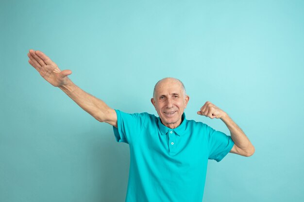 Жест победителя успеха. Портрет кавказского старшего человека на синем фоне студии. Красивая мужская эмоциональная модель. Понятие человеческих эмоций, выражения лица, продаж, благополучия, рекламы. Copyspace.