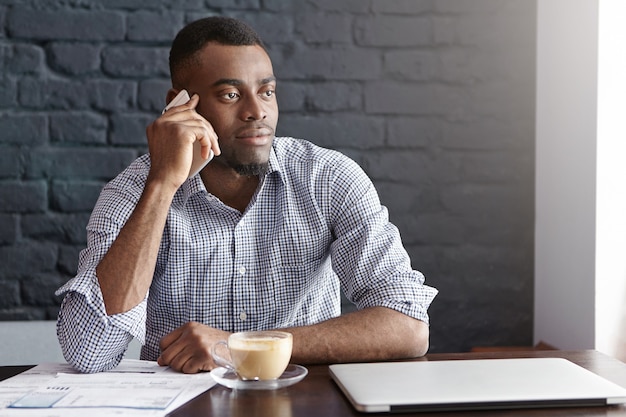 Successful African businessman in shirt with rolled up sleeves having phone call