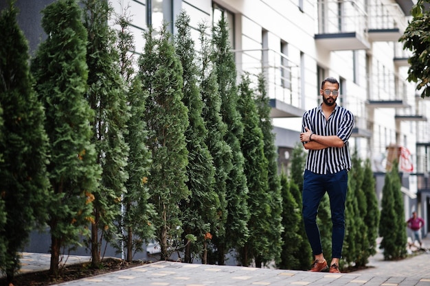 Успешный араб в полосатой рубашке и солнцезащитных очках позирует на улице