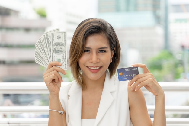 Успешная красивая азиатская бизнес-леди, держащая деньги долларовые банкноты и кредитную карту в руке