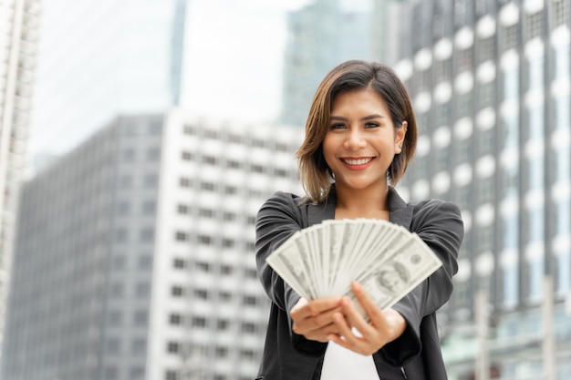 Успешная красивая азиатская бизнес-леди держа деньги долларовые банкноты в руке, концепцию дела