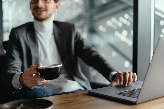 Успешный бизнесмен работает на ноутбуке, попивая кофе