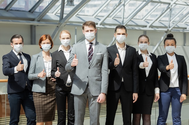 수술용 마스크를 쓰고 함께 서 있는 엄지손가락을 가진 성공적인 사업가들, 의료 및 covid-19 예방 개념