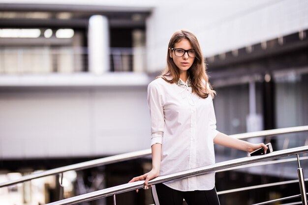 成功したビジネスの女性が休んで立っていると白いtシャツを着たモダンなオフィスセンターのバルコニーを見渡す