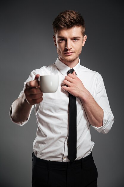 Successful businessman in formalwear holding cup of coffee while standing