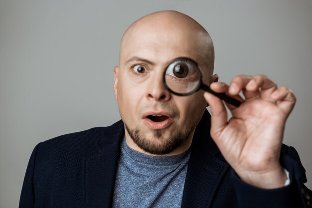 Successful businessman looking through magnifier over beige wall.