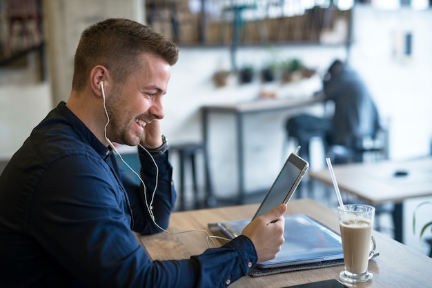 Successful businessman with headphones using tablet in cafe bar