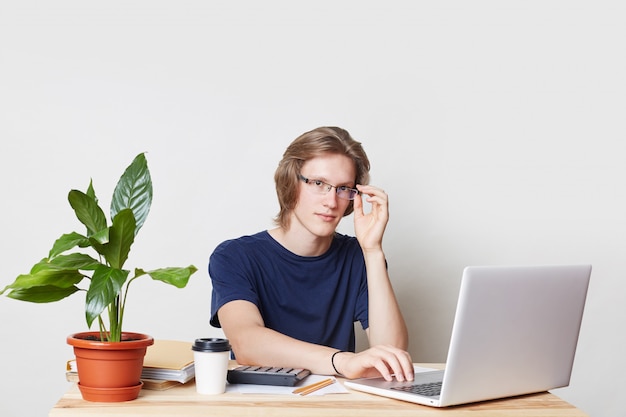 Successful businessman works at home, sits at working place, reads terms of contract, uses laptop computer with free internet connection for productive work. Handsome male creates business plan