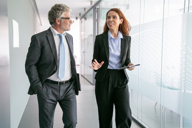 Free photo successful businesspeople walking through office corridor and talking