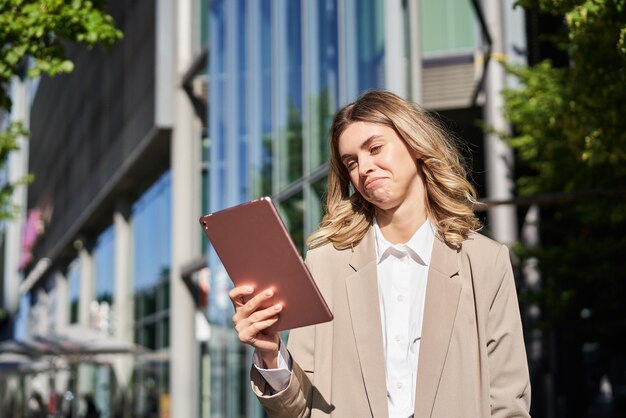 Free photo successful businesswoman checking her work project on way to office standing on street with digital